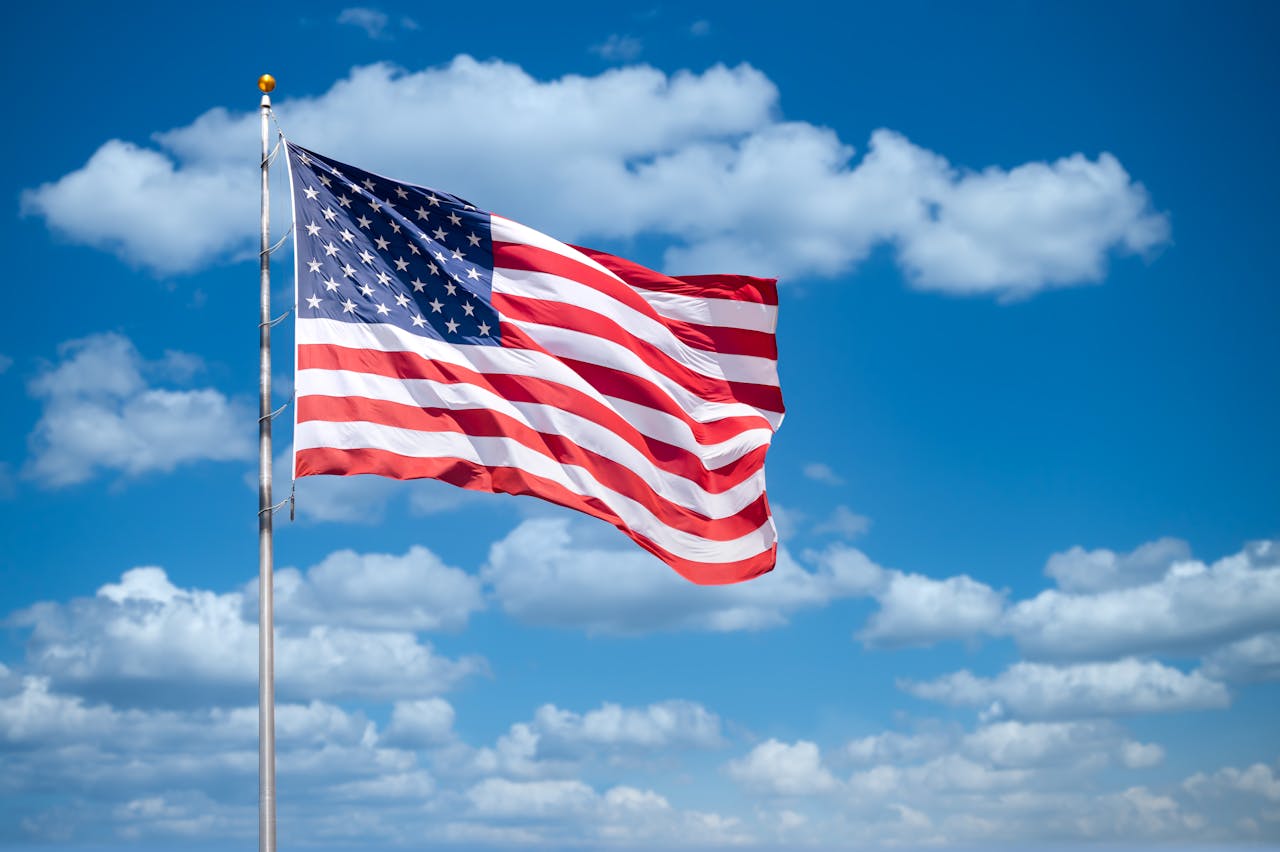 creative Vibrant American flag flying with a bright blue sky and fluffy clouds in the background.